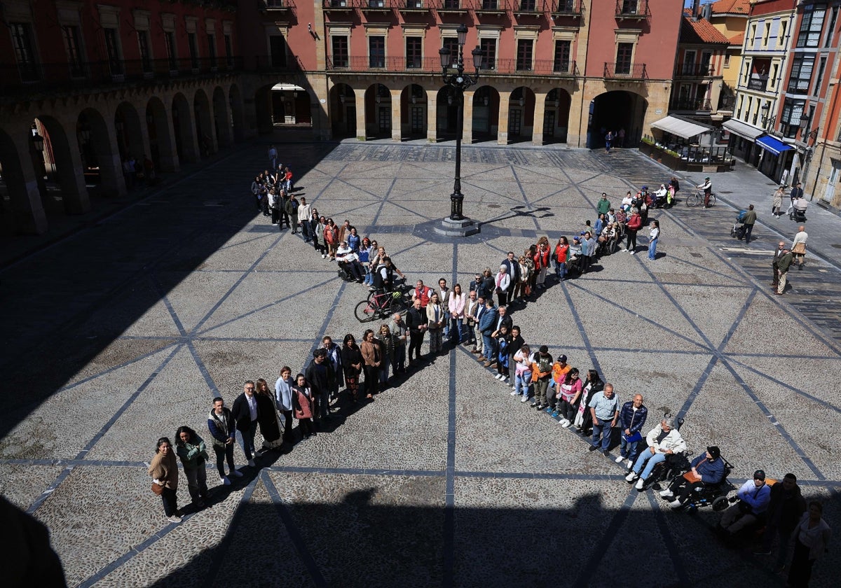 Decenas de personas forman una equis solidaria en la plaza Mayor de Gijón.
